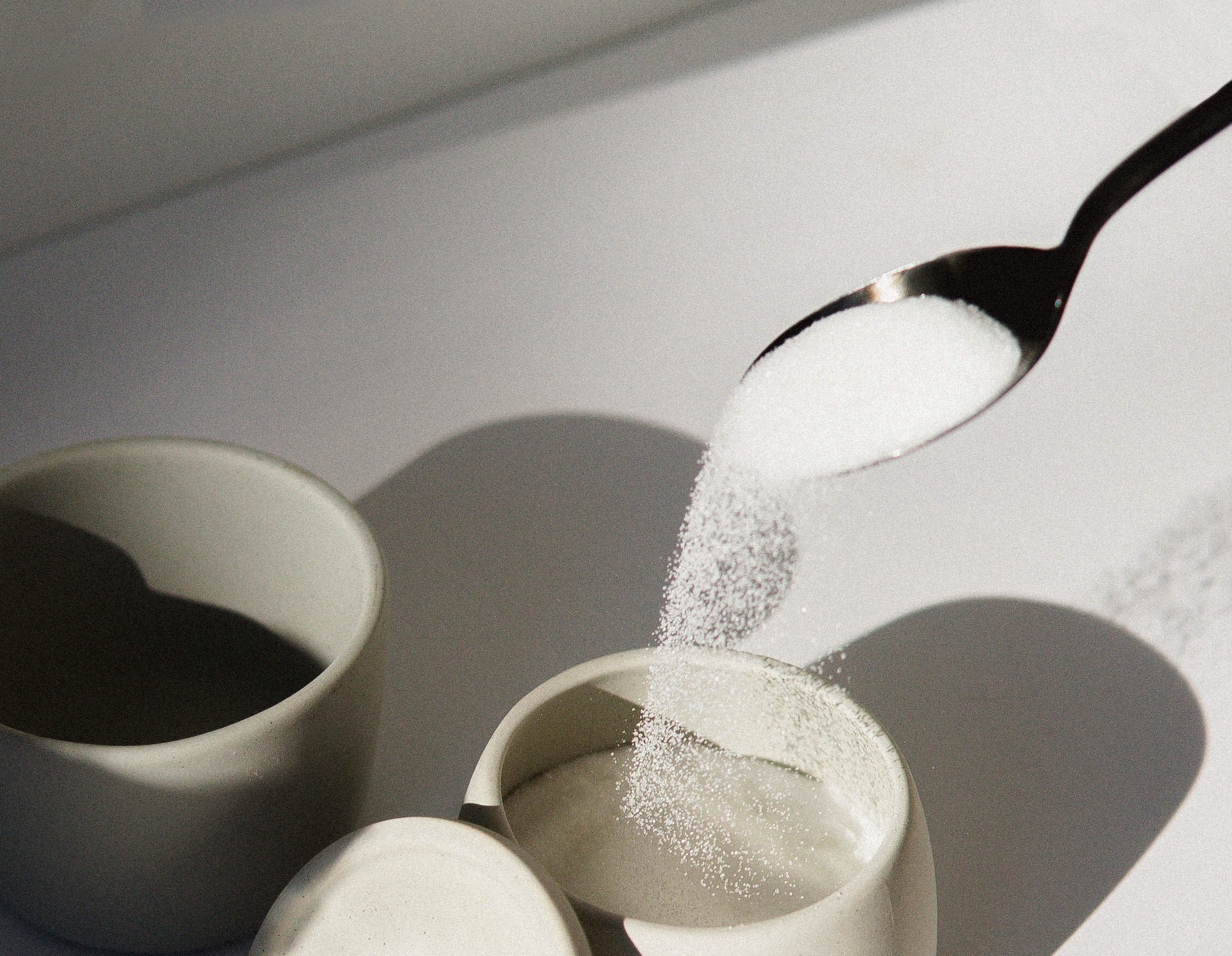Spoon pouring surgar into a sugar bowl.